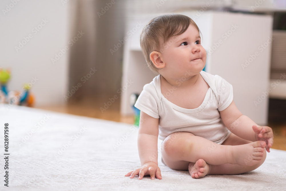 Chubby little boy in white bodysuit sitting on fluffy rug laid on floor in nursery barefoot baby looking at mother relaxing at home happy childhood and development Chubby little boy in white bodysuit sitting on fluffy rug laid on floor in nursery barefoot baby looking at mother relaxing at home happy childhood and development