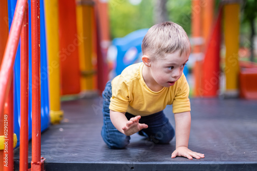 Curious preschooler with Down syndrome sitting on colorful climber at modern playground in residential complex blond kid enjoying outdoor activities in city photo