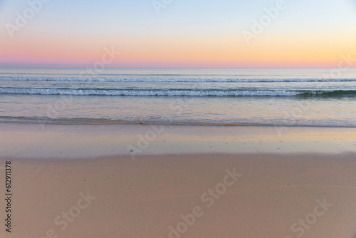 Waves of the sea from the beach at sunset, with shades of color in the sky