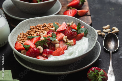 Granola with yogurt and strawberries in a plate on a dark background