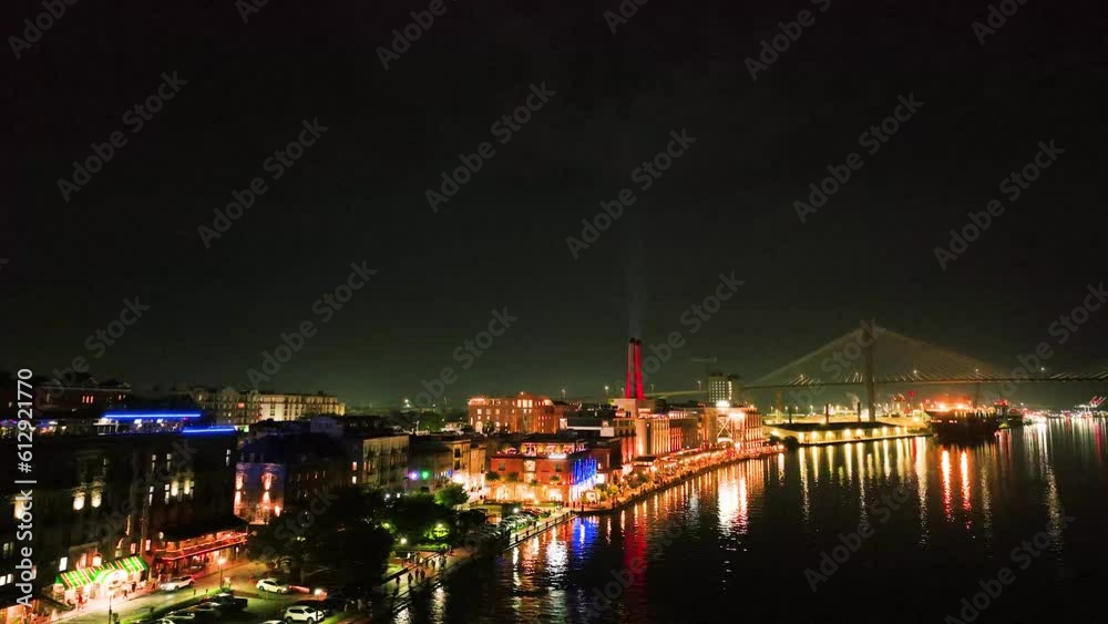 Drone photo at night over the Savannah River. Flying over ferry boat a brightly lit boardwalk with moon in distance. Drone photo at night over the Savannah River. Flying over ferry boat a brightly lit boardwalk with moon in distance.