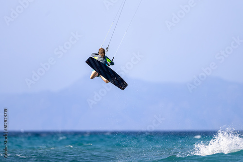 Kitesurfing girl jumping high in turquoise waters with mountains in the background