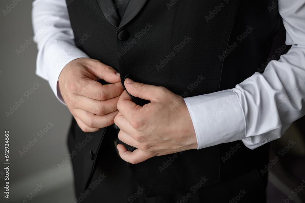 Obraz premium Portrait of a fashionable man fastening a button on jacket, close-up.Wedding day. Young modern businessman.