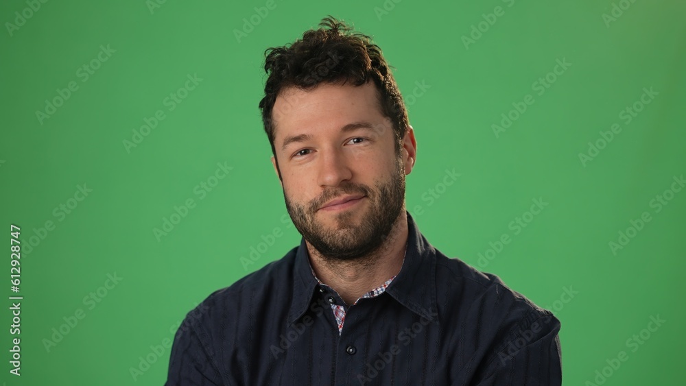 Fototapeta premium Handsome dreamful bearded young guy 20s in hoodie isolated on green screen chroma key background in studio. People sincere emotions, lifestyle concept. Smiling looking at the camera.