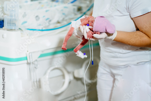 Doctor in ICU examining premature born child. Female nurse with premature born baby in intensive care unit holding infant in her hands.