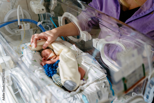 Unrecognizable mother touch and care premature baby placed in a medical incubator. Neonatal intensive care unit in hospital.