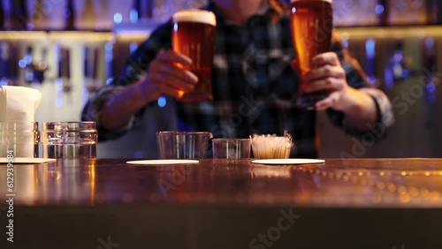 Young man, bartender serving two glasses of chill lager beer at bar, pub. Unfocused image of man smiling. Concept of alcohol drink, party, taste, relaxation, brewery. Ad photo