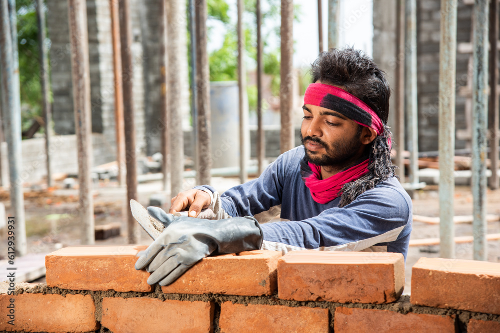 Obraz premium Happy Indian male construction worker constructing brick wall - hard working concept, manual labour