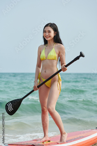 Happy fit young woman in yellow bikini paddleboarding on sunny day