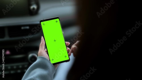 Close up of a woman's hand using a smartphone in the car. Mobile phone green screen display in car for app. Mockup.