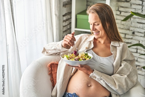 Pregnant woman savors salad in serene, diffused light