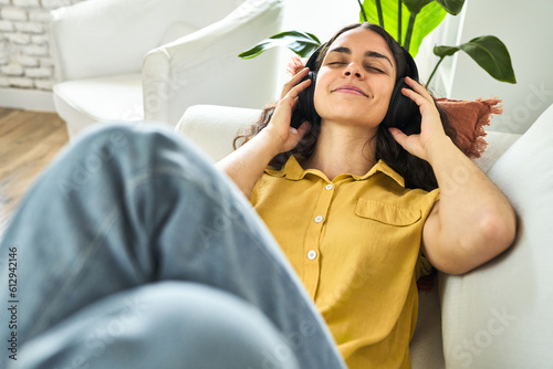 Bilde på lerret A young woman, lying on the sofa, blissfully immersed in the soothing melodies of her headphones on a relaxing morning
