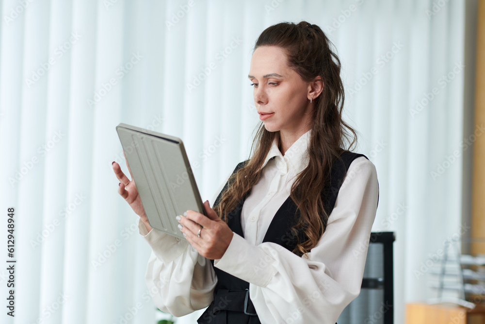 Young businesswoman working online on digital tablet while standing in office Young businesswoman working online on digital tablet while standing in office