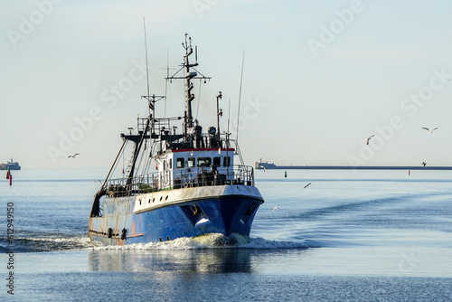 A small fishing vessel returns after fishing to the port, beautiful view with blue sky and seagulls