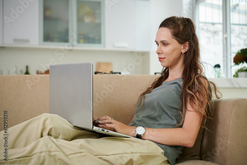 Young woman sitting on sofa and using laptop during her leisure time at home