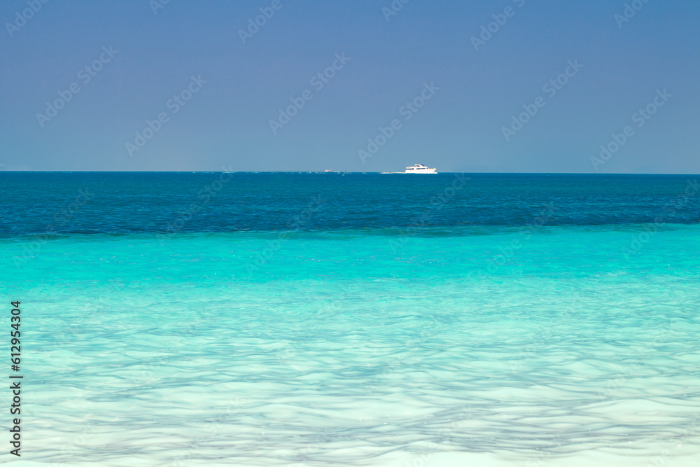 Sea, turquoise clear water, white boat floating in distance