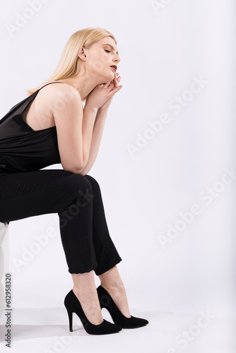 Portrait of a young and elegant girl sitting on a pouf on a white background.