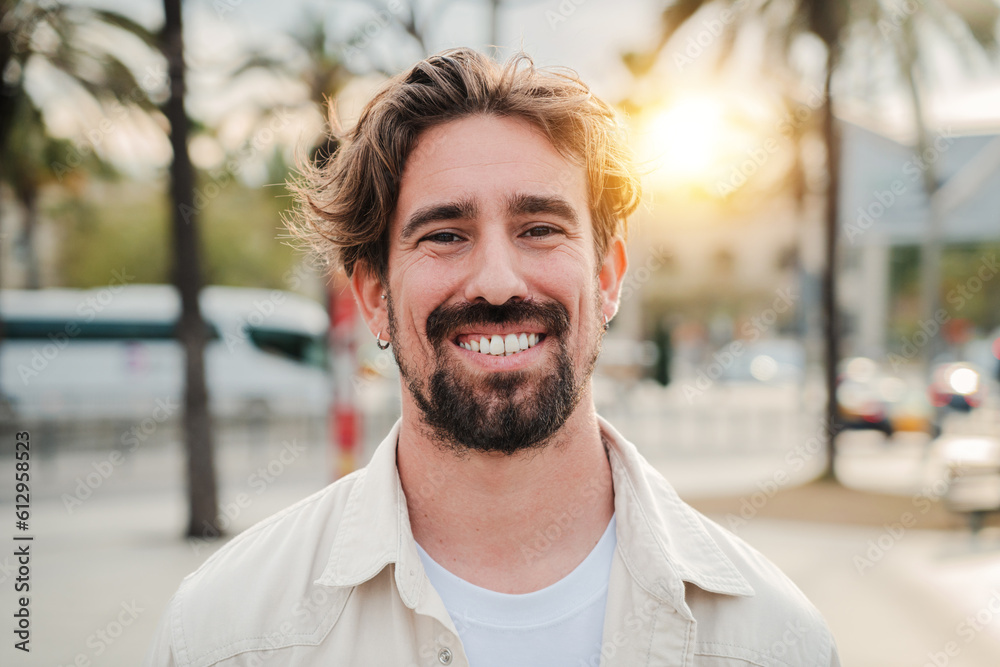 Close up portrait of handsome bearded guy with perfect white teeth smiling and looking at camera standing outdoors. Front view of young adult man with friendly and positive expression. Happy male Close up portrait of handsome bearded guy with perfect white teeth smiling and looking at camera standing outdoors. Front view of young adult man with friendly and positive expression. Happy male