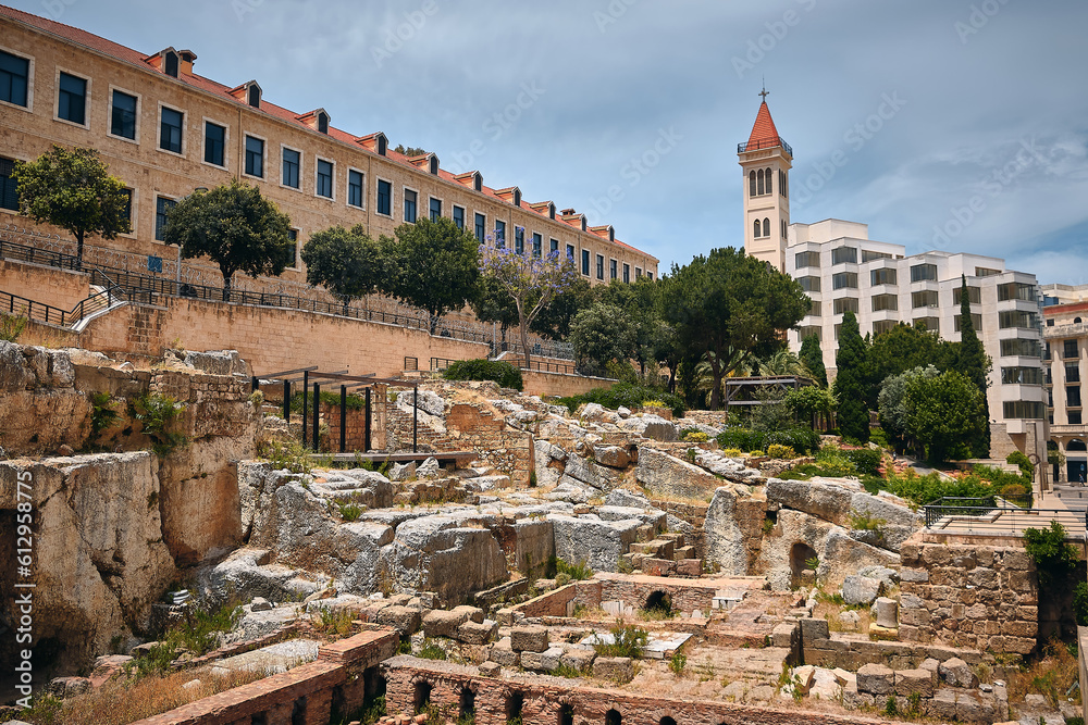 Obraz premium Ruins of Roman bath surrounded by modern buildings of Downtown Beirut. Roman Baths of Berytus, ancient archaeological site. Grand Palace and Saint Louis Des Capucins cathedral at background