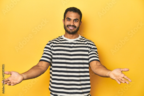 Casual young Latino man against a vibrant yellow studio background, showing a welcome expression.