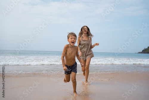 Beautiful boy with mom run at beach after swimming in sea at sunny day
