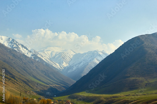 landscape against a mountain backdrop of high mountain ranges with snow-capped mountains and a blue sky with clouds © justoomm