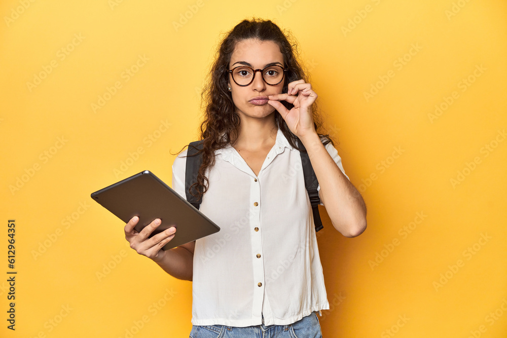 Student holding a tablet, glasses, backpack on, with fingers on lips keeping a secret.