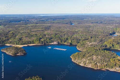 Aerial drone view of circle sea fish farm cages and round fishing nets, farming salmon, trout and cod, feeding the fish a forage, with Scandinavian lake landscape and forest island, a summer day