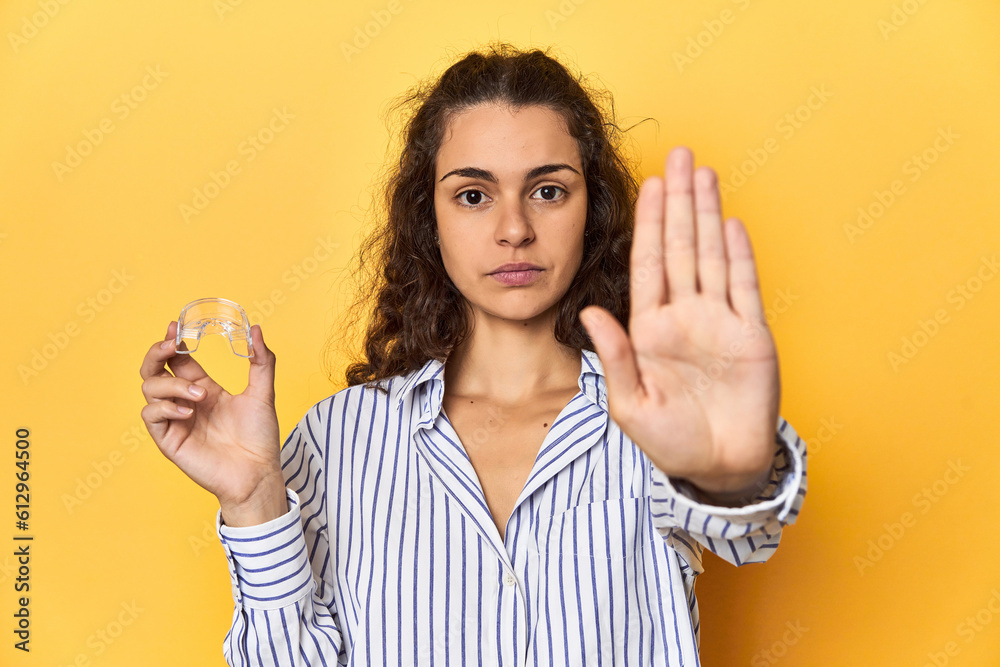 Woman holding an invisible teeth corrector standing with outstretched hand showing stop sign, preventing you. Woman holding an invisible teeth corrector standing with outstretched hand showing stop sign, preventing you.