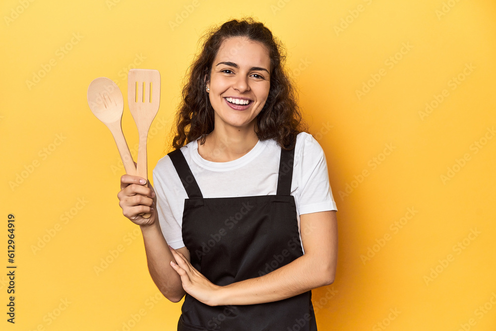 Woman with apron, wooden cooking utensils, yellow, laughing and having fun. Woman with apron, wooden cooking utensils, yellow, laughing and having fun.