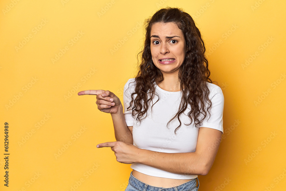 Young Caucasian woman, yellow studio background, shocked pointing with index fingers to a copy space.