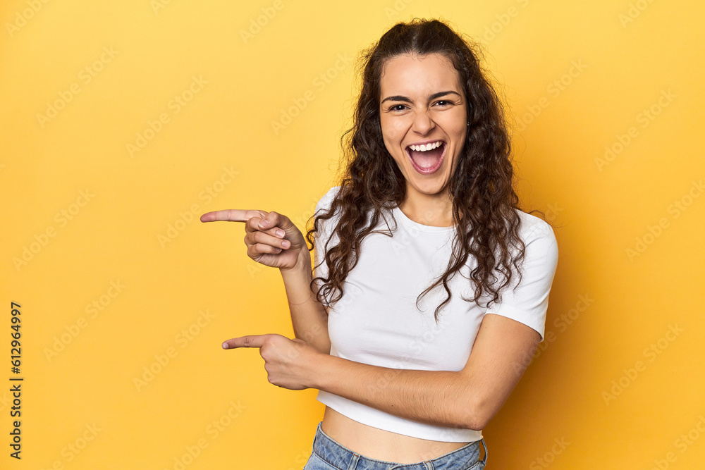 Young Caucasian woman, yellow studio background, pointing with forefingers to a copy space, expressing excitement and desire.
