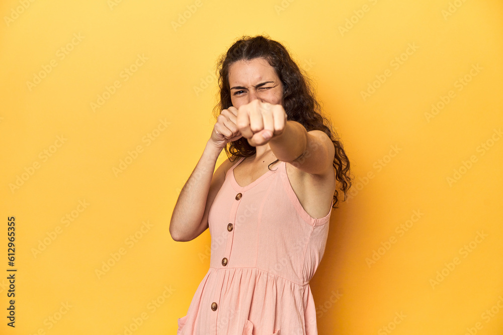 Obraz premium Young Caucasian woman, yellow studio background, throwing a punch, anger, fighting due to an argument, boxing.