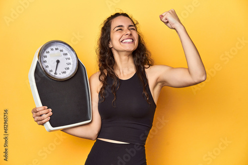 Young Caucasian woman with scale, weight management concept, yellow background. photo