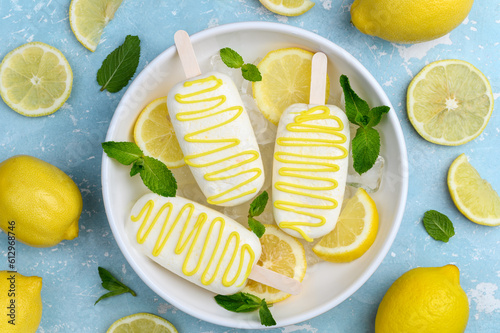 Lemon yogurt ice cream on a stick in a white plate with ice, lemon slices and mint  on a blue background. Top view