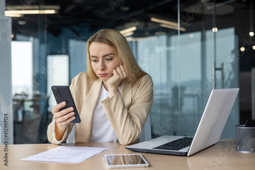 Sad and disappointed woman received bad news online, business woman at workplace inside office in depression reading bad news using app on smartphone, female worker with phone in hands thoughtful