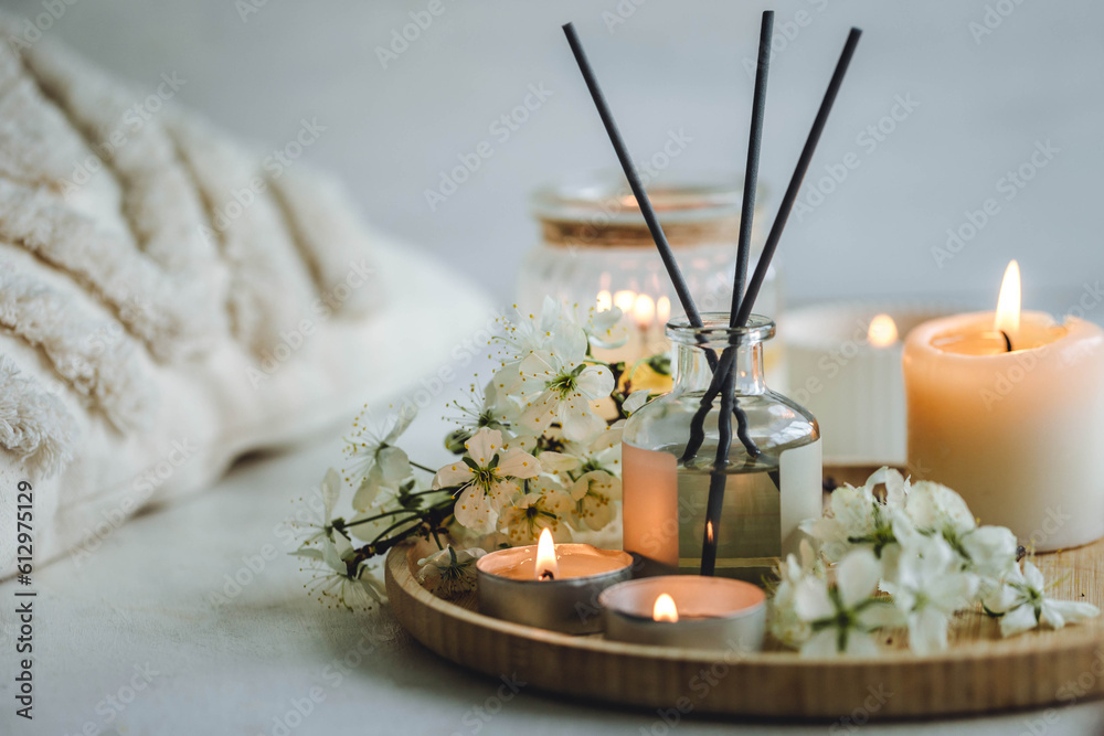 Cozy home decor, hygge and aromatherapy concept. Comfortable atmosphere, spring delicious fresh smell. Aroma diffuser, burning candle, cherry blooming flowers and perfume on wooden bamboo tray.