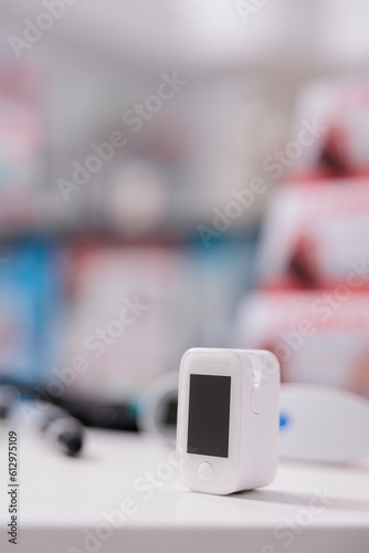 Medical oximeter standing on table in empty pharmacy ready to be used by customer, digital device to measure oxygen saturation. Drugstore filled with drugs, vitamins and pharmaceutical products