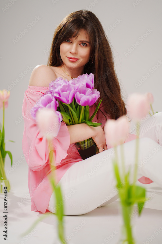 beautiful brunette woman with long hair sits on the floor with vases of flowers 