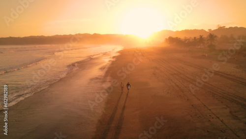 AERIAL Sporty couple with surfboards walking on beach in incredible sunset light