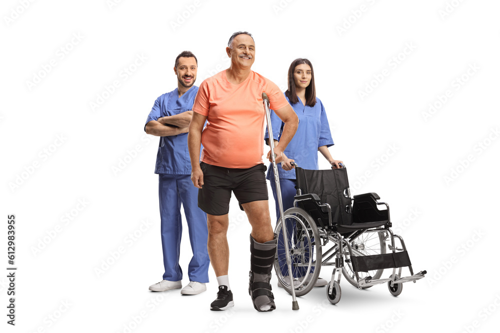 Mature male patient with an orthopedic boot and crutch standing with health care workers