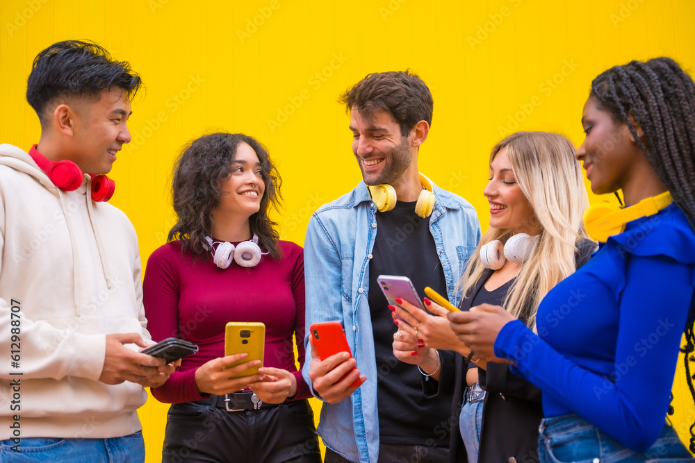 Obraz premium Low angle view of a group of smiling young multi ethnic teenage friends using cell phones on a yellow background. Technology addicted millennial community concept. Social Media communication