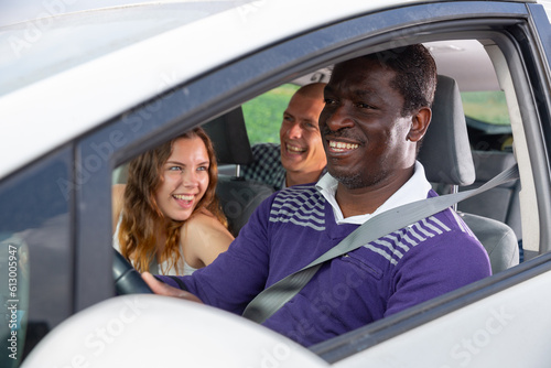 Portrait of laughing african american man driving car with cheerful fellow travelers in passenger seats. Friendly road trip and travel concept © JackF