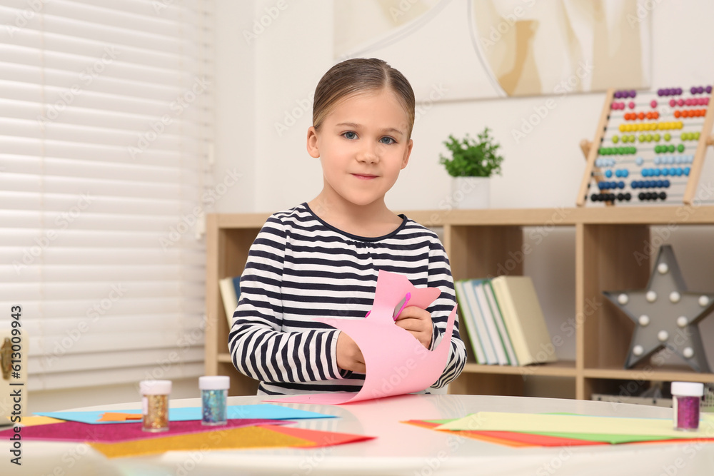 Cute little girl cutting pink paper at desk in room. Home workplace Cute little girl cutting pink paper at desk in room. Home workplace
