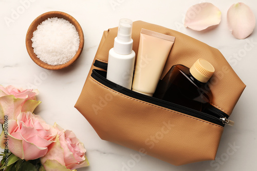 Preparation for spa. Compact toiletry bag, flowers and different cosmetic products on white marble table, flat lay
