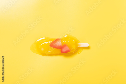 top view mango fruit flavor with strawberry slices popsicle in a melting process on yellow background