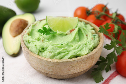 Bowl of delicious guacamole and ingredients on table, closeup