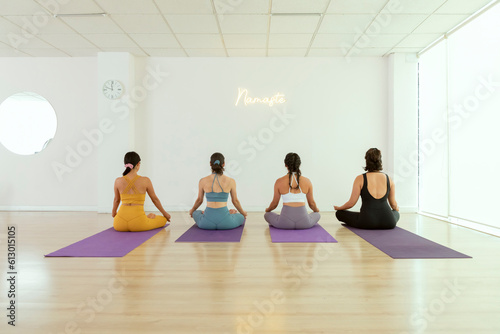 A group of young women practicing yoga are sitting with their backs to the camera in lotto flower pose