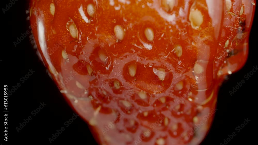 Honey trickles down the strawberry. Macro slider shot on a black background.