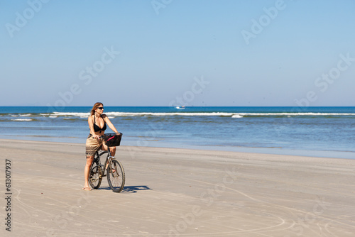 beautiful woman over 40 years old riding a bicycle on the beautiful beach of Itaguaré and Guaratuba. Woman practicing physical activity on the empty beach.